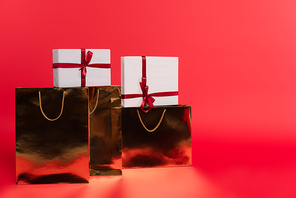 Gifts in golden shopping bags on red background