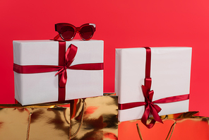 Sunglasses on present near shopping bags isolated on red