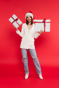 Smiling woman in santa hat holding gift boxes on red background