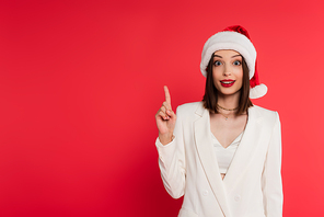 Excited woman in santa hat having idea isolated on red
