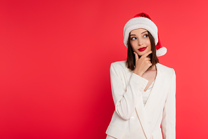 Thoughtful woman in jacket and santa hat isolated on red