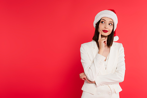 Pensive woman in santa hat and white jacket looking away isolated on red