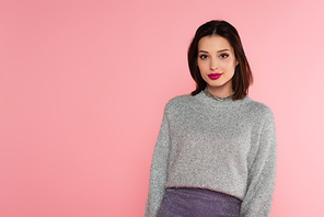 Pretty woman in sweater looking at camera isolated on pink