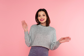 Smiling woman in warm sweater waving at camera isolated on pink