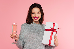 Pretty woman with champagne and gift looking at camera isolated on pink