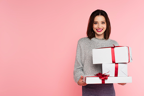 Pretty woman smiling at camera while holding gift boxes isolated on pink