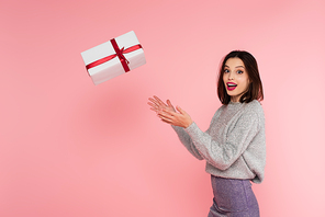 Excited stylish woman throwing gift box isolated on pink
