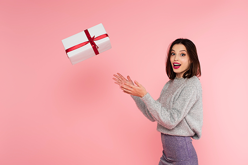 Excited stylish woman throwing gift box isolated on pink