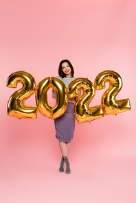 Stylish woman smiling near balloons in shape of 2022 numbers on pink background