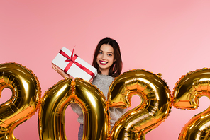 Happy woman holding present near balloons in shape of 2022 numbers isolated on pink