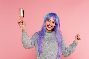 Positive stylish woman with dyed hair holding champagne isolated on pink