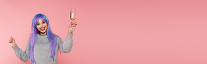 Cheerful woman with dyed hair holding glass of champagne isolated on pink, banner