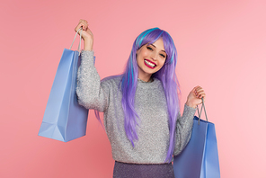 Stylish woman with dyed hair holding shopping bags isolated on pink