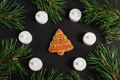 top view of gingerbread cookie near candles and pine branches on black