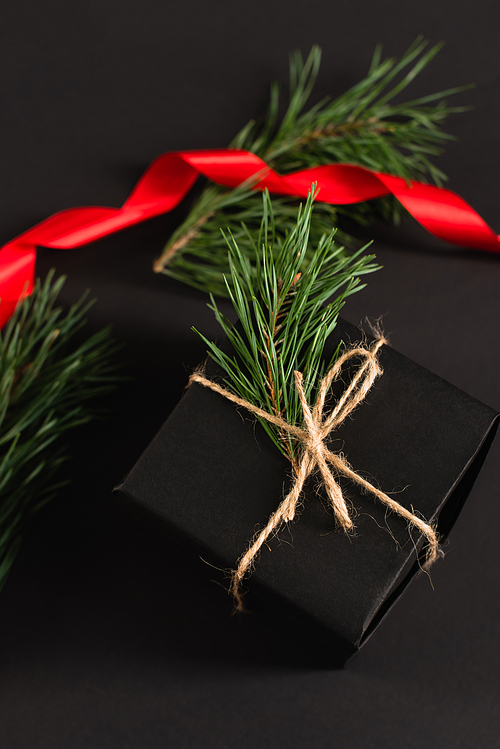 top view of gift box with fir branch near blurred red ribbon on black