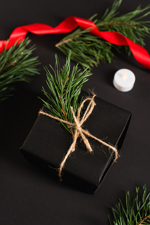 top view of gift box with fir branch near candle and blurred red ribbon on black