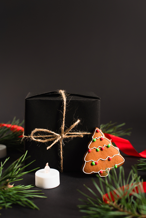 wrapped present near fir branches, gingerbread cookie and candle on black