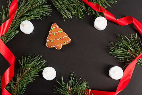 top view of gingerbread cookie near candles, fir branches and red ribbon on black