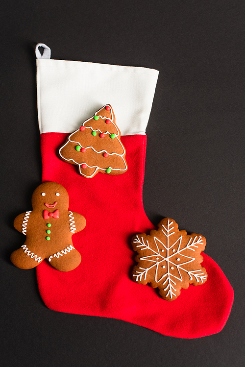 top view of different shapes gingerbread cookies on red christmas stocking isolated on black