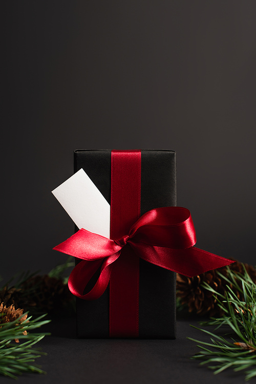 wrapped present with red ribbon and blank card near blurred fir branches on black