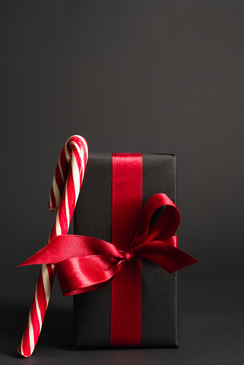 striped candy cane near wrapped present with red ribbon on black