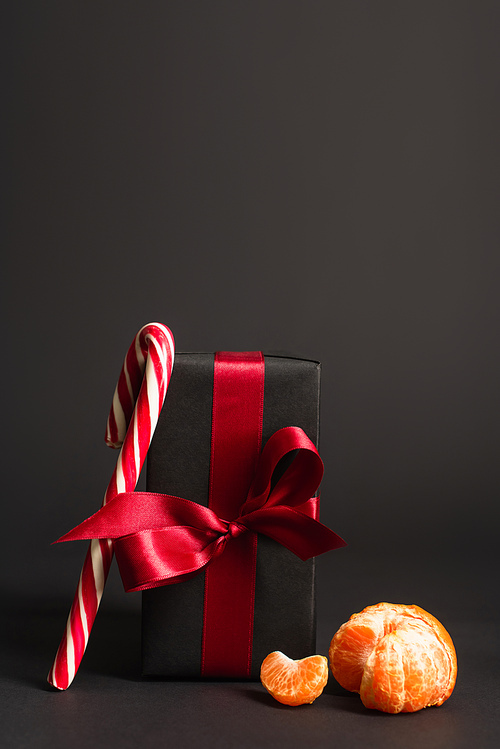 striped candy cane near wrapped present with red ribbon and tangerine on black