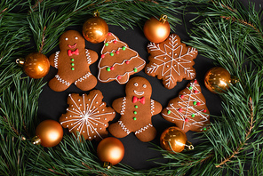 top view of gingerbread cookies near golden christmas balls near fir branches on black