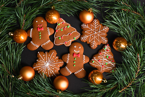 top view of gingerbread cookies near golden christmas balls near fir branches on black