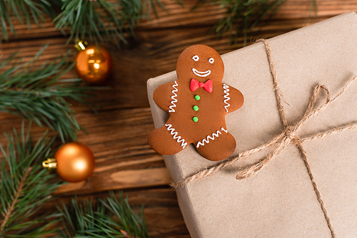 top view of gingerbread cookie on gift box near blurred pine branches on wooden surface