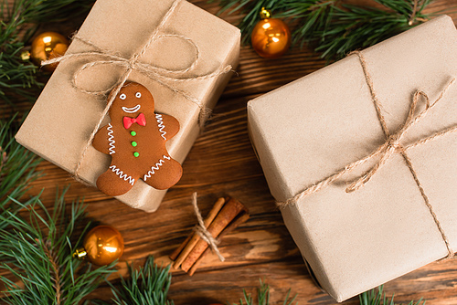 top view of gingerbread cookie on gift box near blurred pine branches and cinnamon sticks on wooden surface