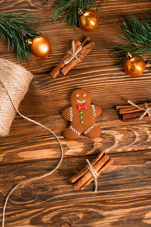 top view of gingerbread cookie, cinnamon sticks and fir branches on wooden surface