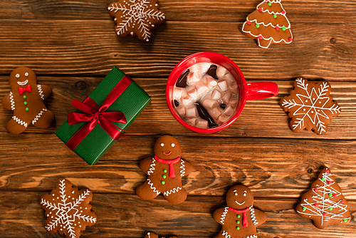 top view of cup of cocoa with marshmallows near gift box and gingerbread cookies on wooden surface
