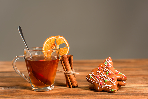 glass cup of tea with sliced orange near cinnamon sticks and gingerbread cookies isolated on grey