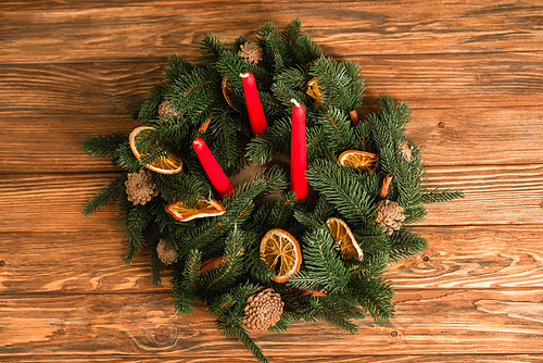top view of christmas wreath with red candles and green fit branches on wooden surface