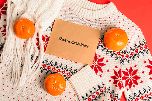 top view of greeting card with merry christmas lettering near tangerines on knitted sweater