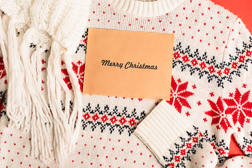 top view of greeting card with merry christmas lettering on knitted sweater near scarf