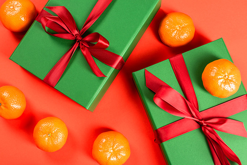 top view of green wrapped presents near ripe tangerines on red background