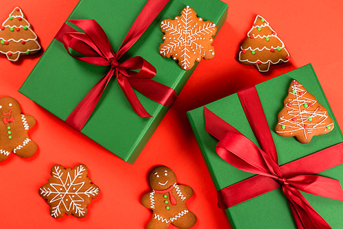 top view of green wrapped presents near gingerbread cookies on red background
