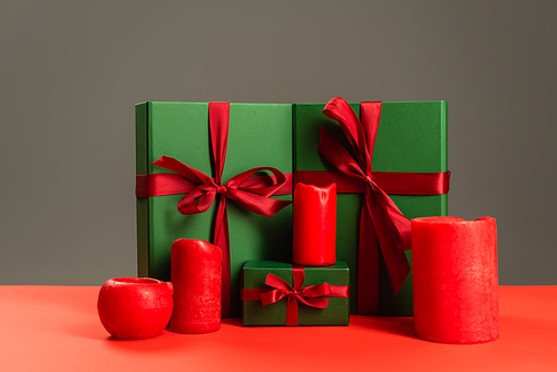 red candles near green wrapped presents isolated on grey