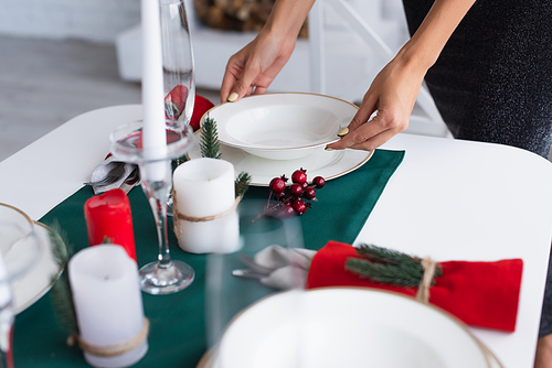 cropped view of woman holding white plate while serving festive table