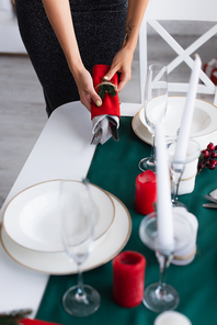 partial view of woman holding cutlery wrapped in festive napkins while serving table
