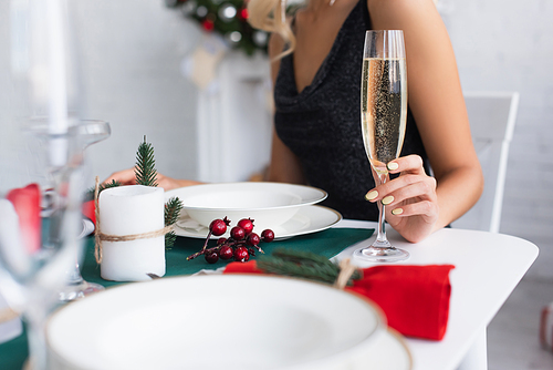 partial view of woman with glass of champagne sitting at festive table
