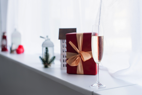 selective focus of red gift box near blurred decorative house model on windowsill
