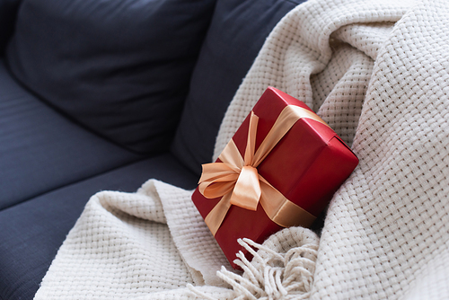 sofa with soft blanket and red gift box decorated with ribbon