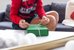 cropped view of woman tying decorative ribbon on gift box near blurred christmas balls