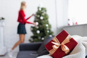 selective focus of gift box with decorative ribbon near woman and christmas tree on blurred background