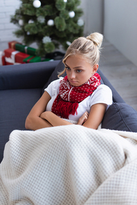 high angle view of sick and upset woman with crossed arms on sofa near christmas tree on blurred background