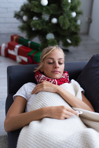 sick woman sleeping on sofa near presents and christmas tree on blurred background
