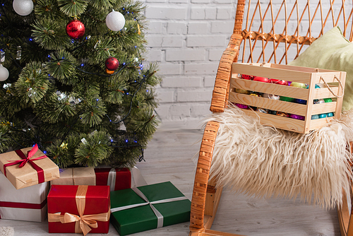 wooden box with decorative baubles on wicker chair near presents under christmas tree