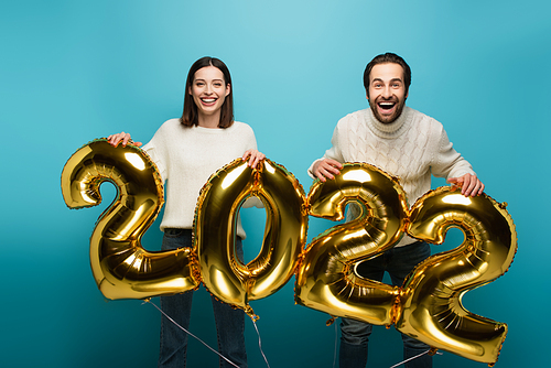 cheerful couple  while holding golden balloons in shape of 2022 on blue